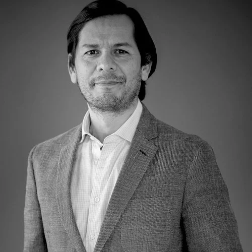 Black and white photo of Alejandro Chavez-Badiola in a suit jacket and collared shirt, smiling slightly.