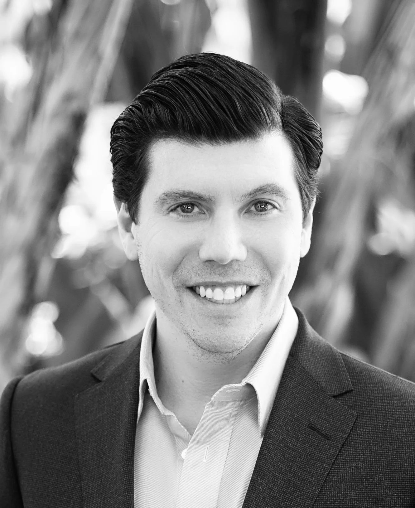 Black and white headshot of Brian Levine, wearing a suit jacket and collared shirt, against a blurred natural background.