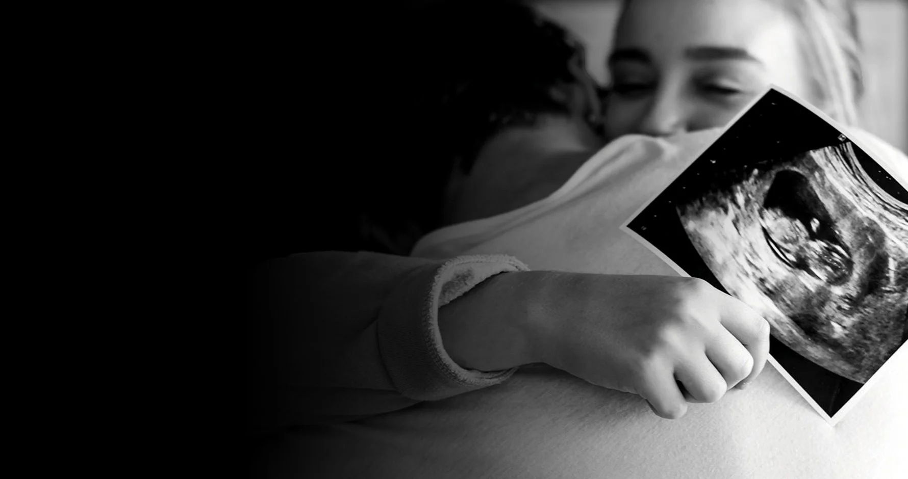 A child hugging an adult while holding an ultrasound image in their hand.