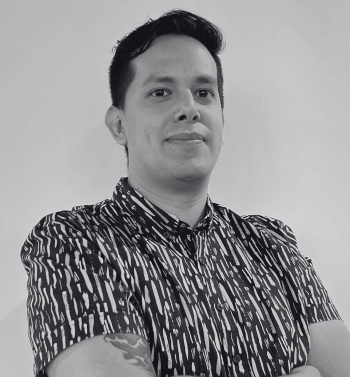 Black and white portrait of César Millan with arms crossed, standing indoors with a neutral background.