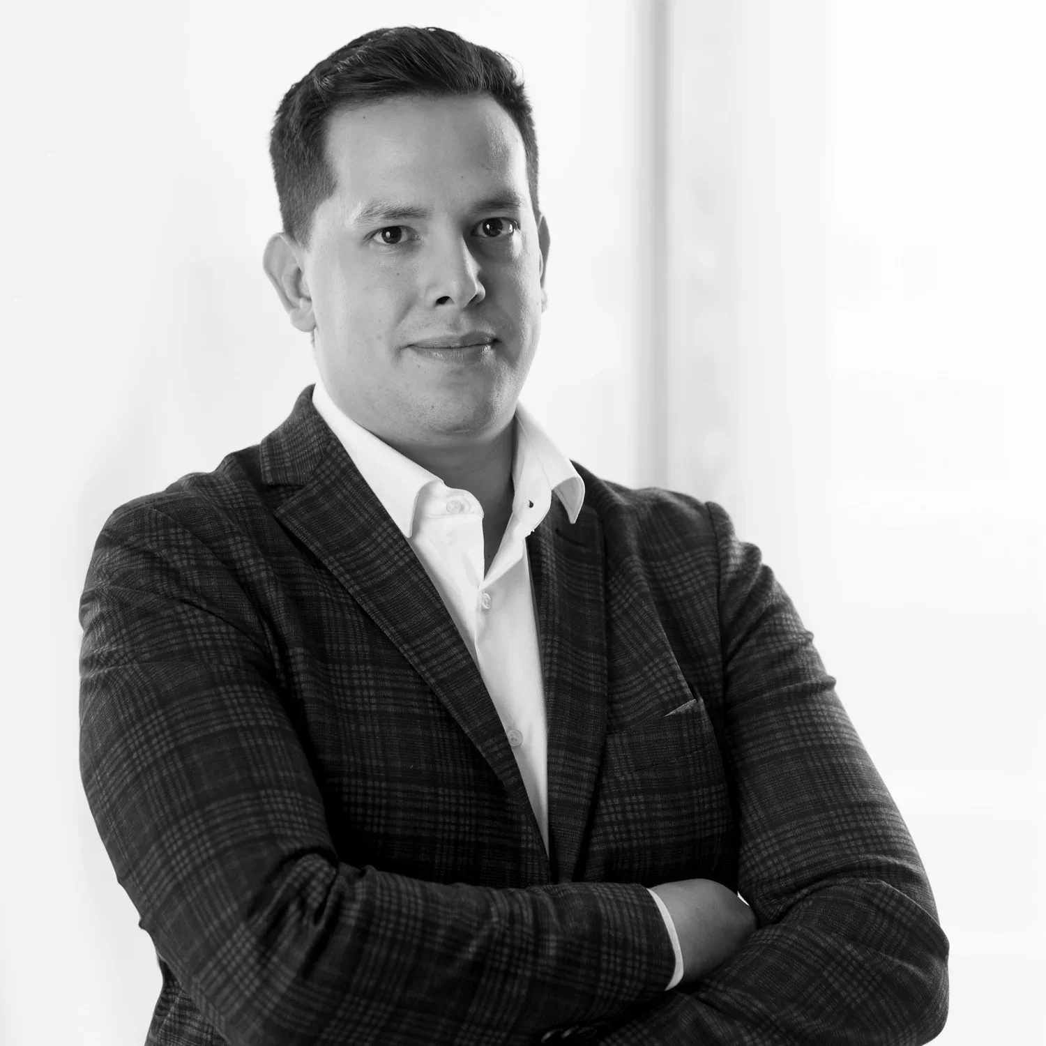 Black and white portrait of César Millan in a suit with arms crossed, standing indoors with a neutral background.