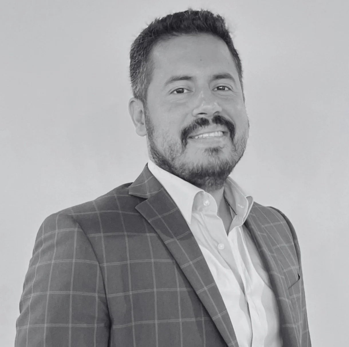 Black and white portrait of César Niebla wearing a suit, smiling, with hands clasped on a table.