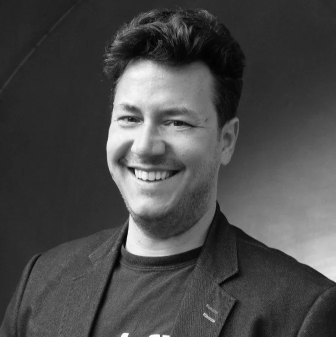 Black and white portrait of Professor Christos Bergeles, wearing a blazer over a t-shirt.