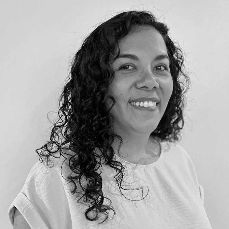 A black-and-white photograph of Evelyn Sanchez smiling at the camera, wearing a light-colored top, against a plain background.