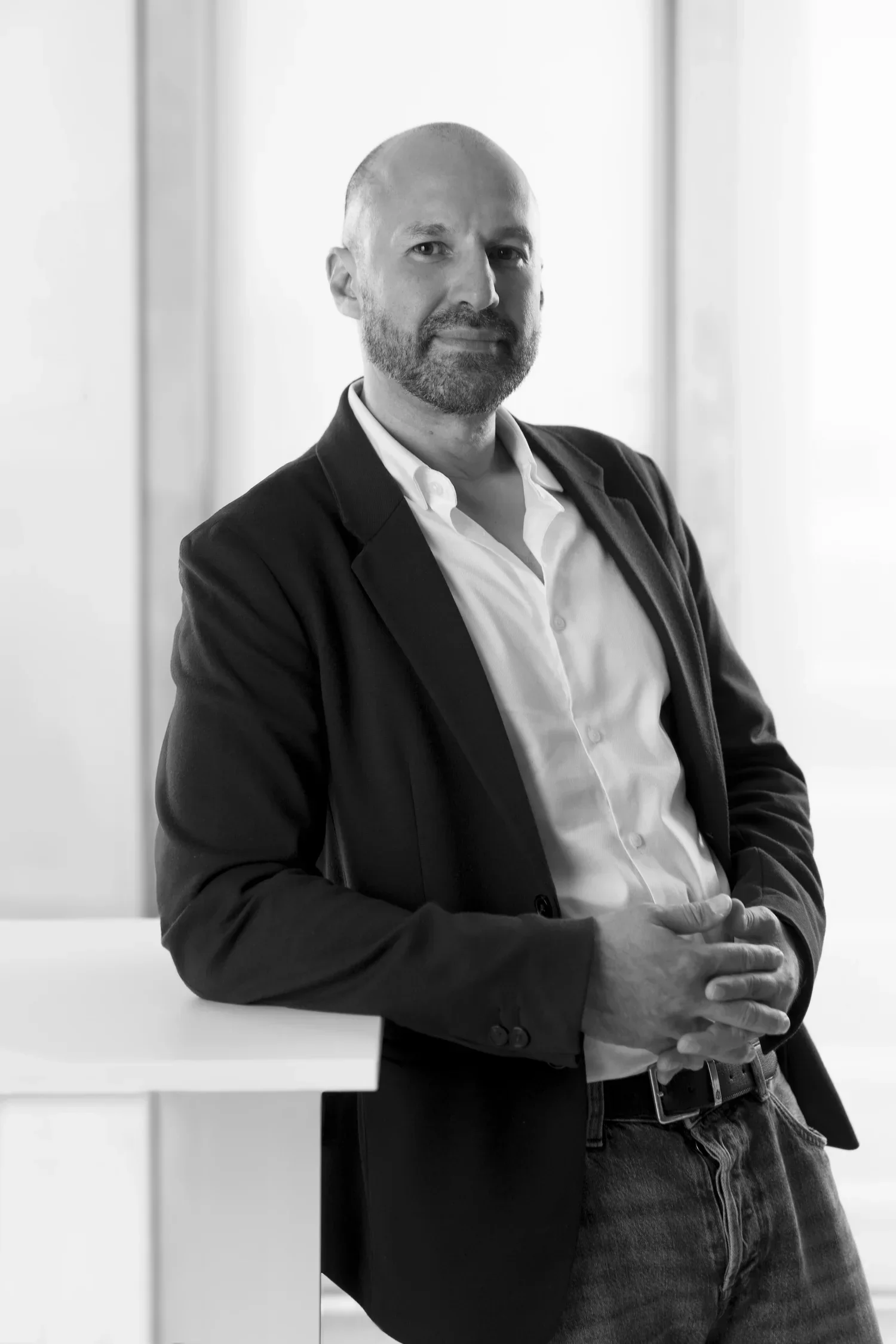 Black and white portrait of Gerardo Mendizabal in business attire, wearing a white shirt and a dark blazer, standing with arms crossed in front of a light-colored background.