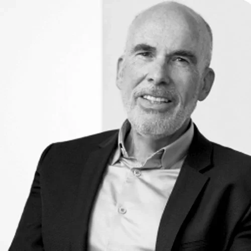 Black and white photo of Jacques Cohen, wearing a suit jacket over a shirt, smiling.