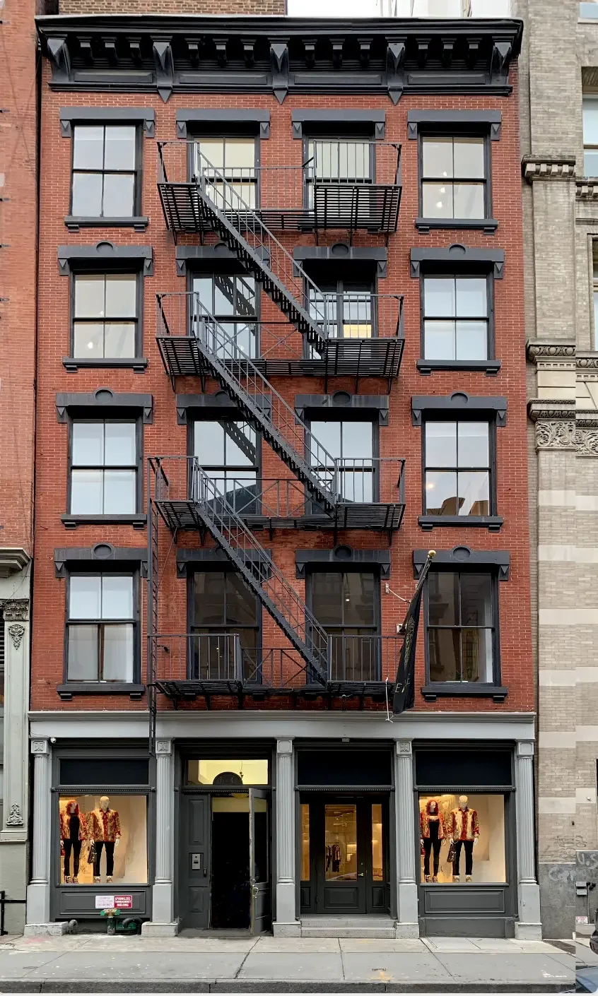Four-story brick building with black window frames and a fire escape on the front facade. The ground floor features a retail store with large display windows and mannequin displays. The building is situated on a city street.