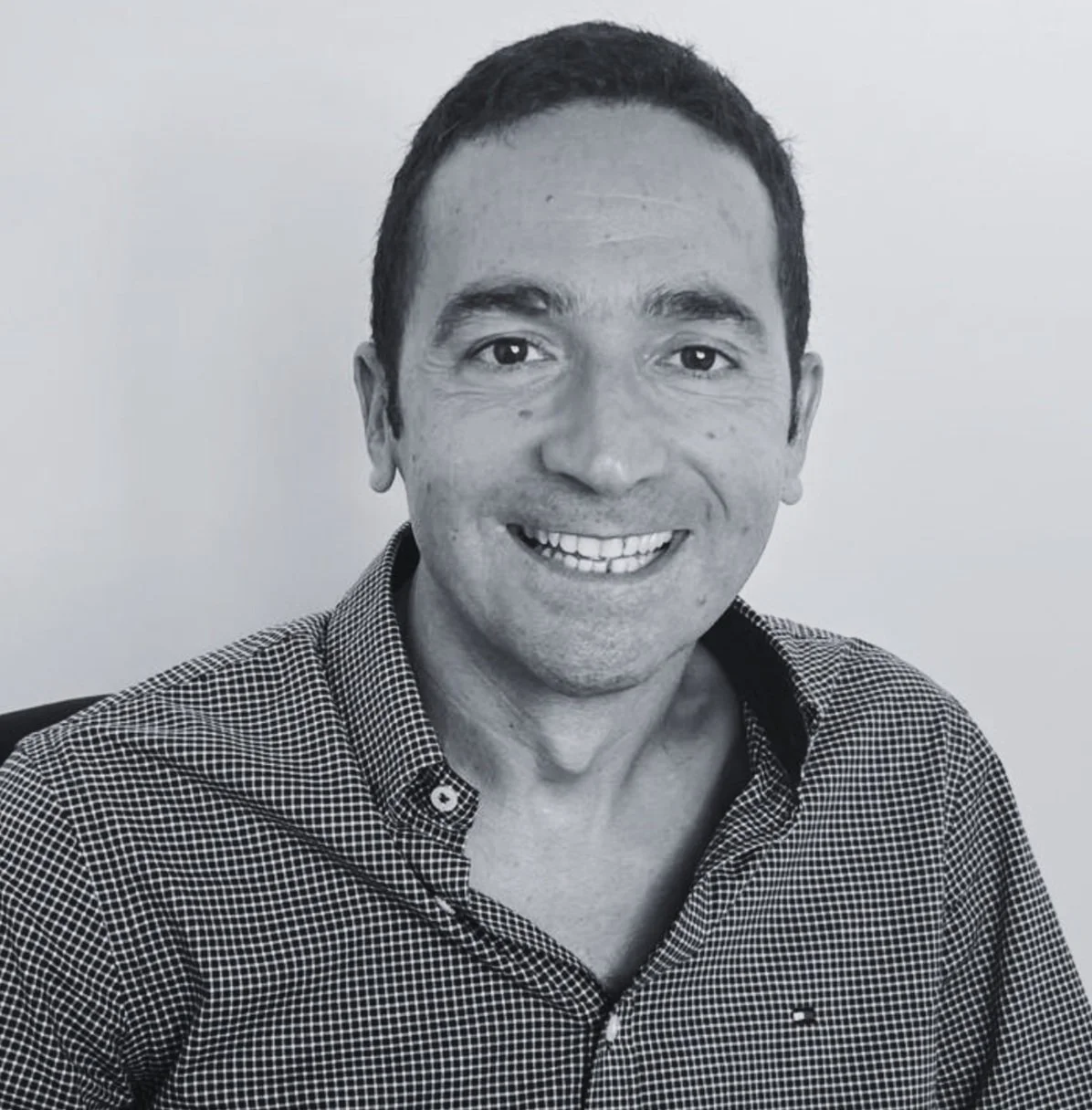 Black and white photo of Nuno Costa-Borges, wearing a checkered shirt, sitting in front of plain background.