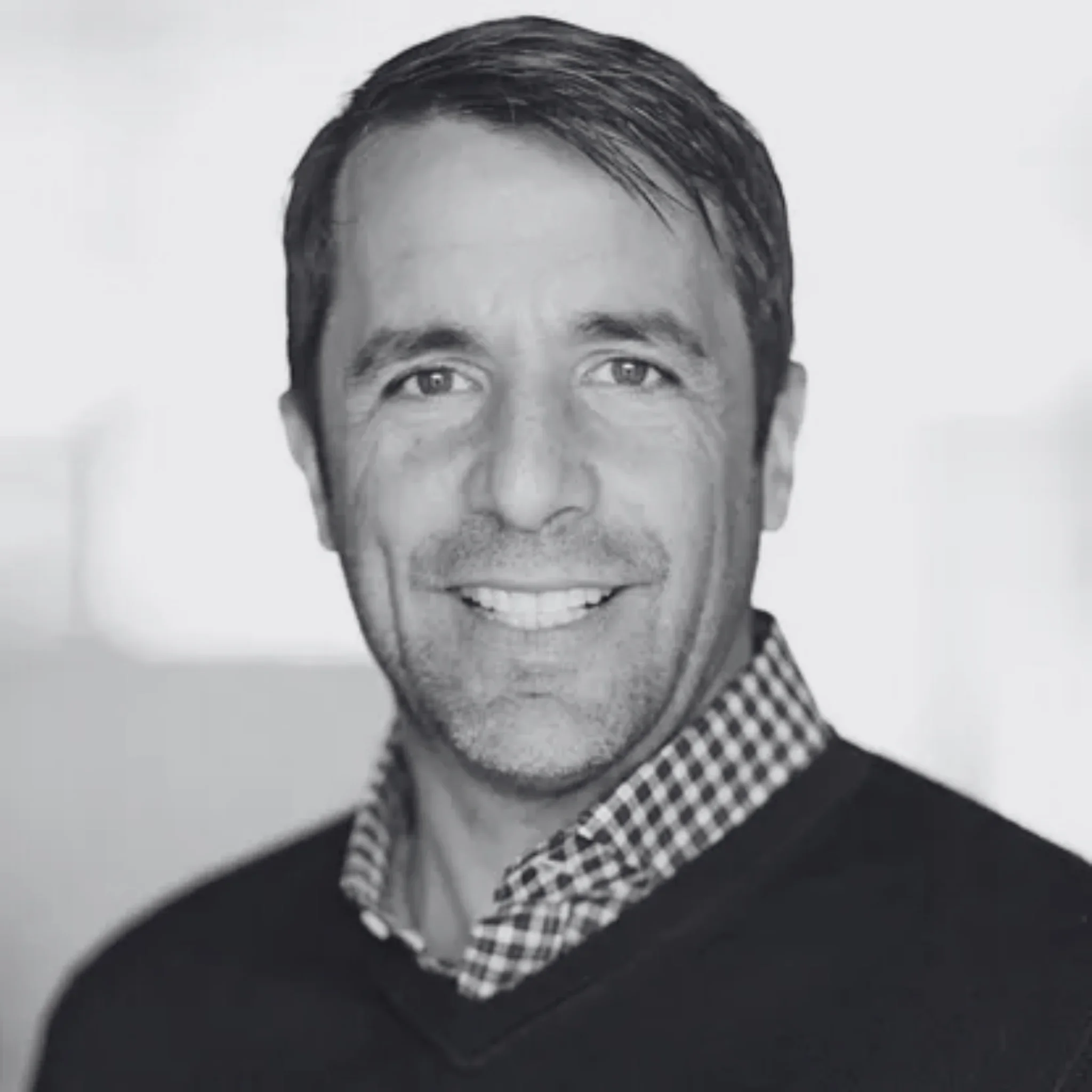Black and white close-up portrait of Stuart Peterson, wearing a checkered shirt under a dark sweater.